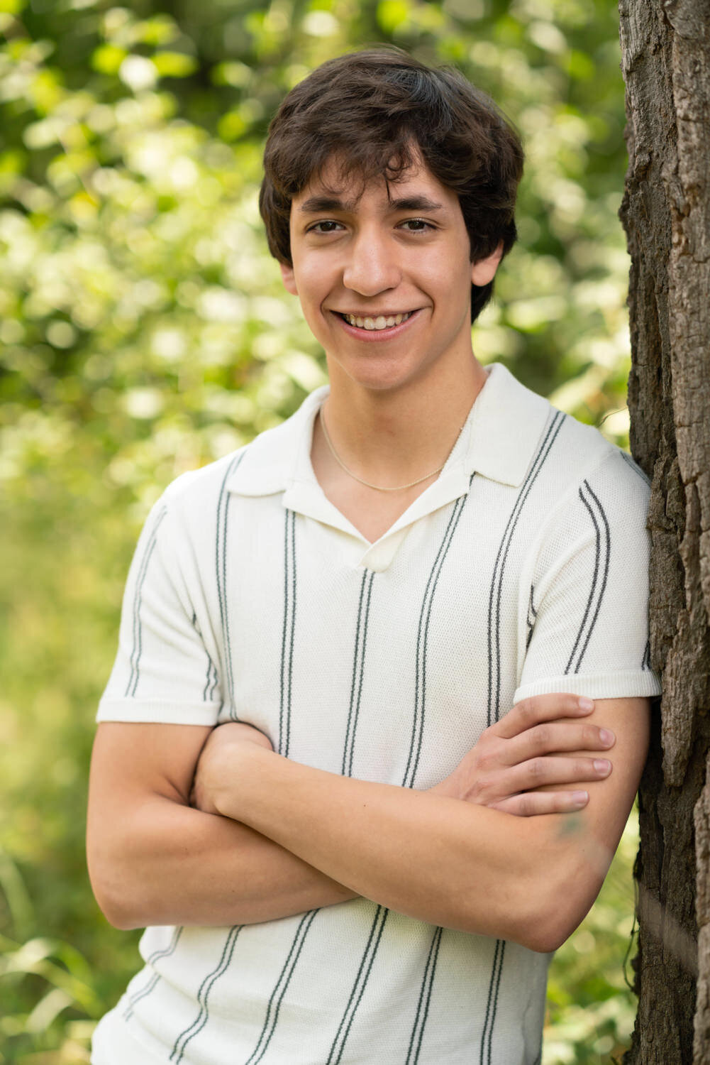 Senior boy in collared shirt smiles while standing against a tree.