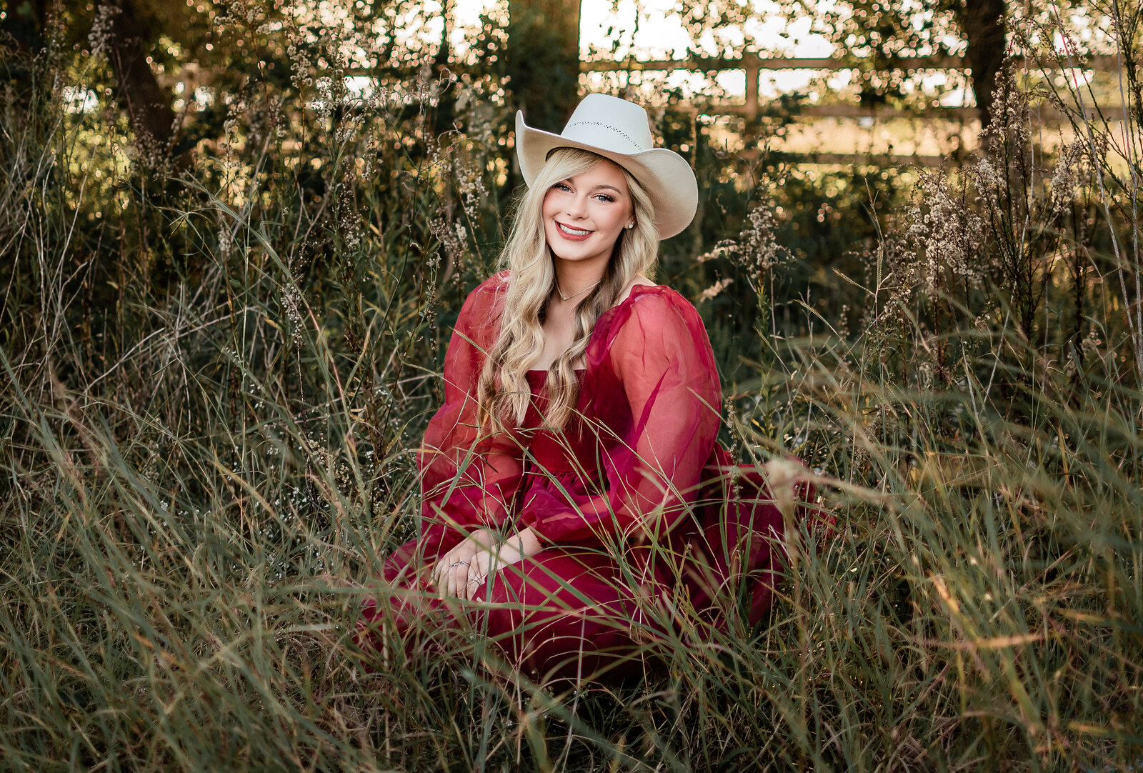 A Friendswood senior in a red dress sits in a field of long grass.