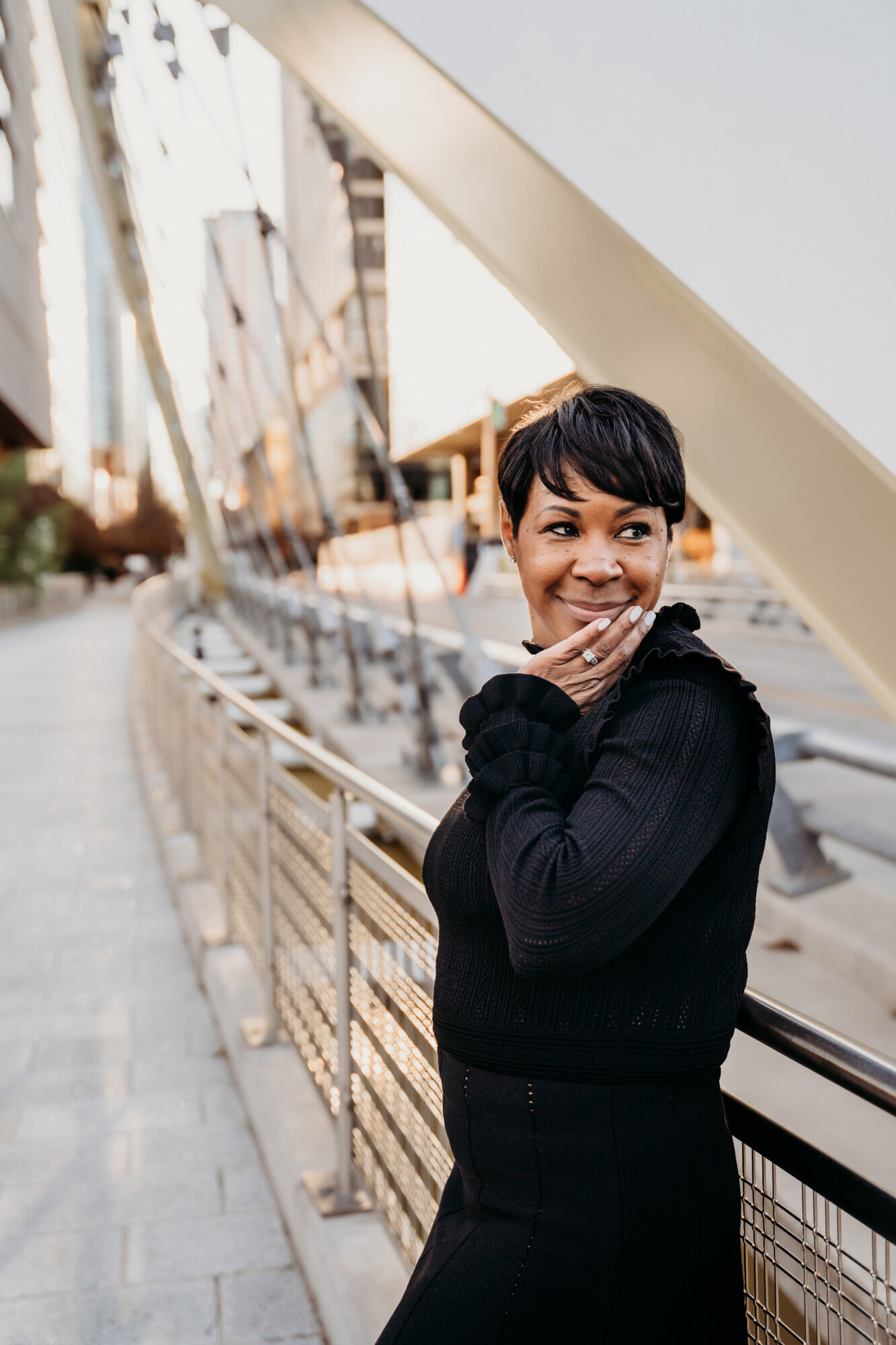 Branding Photographer,  a woman leans on a city bridge's railing, she is all dressed up and happy