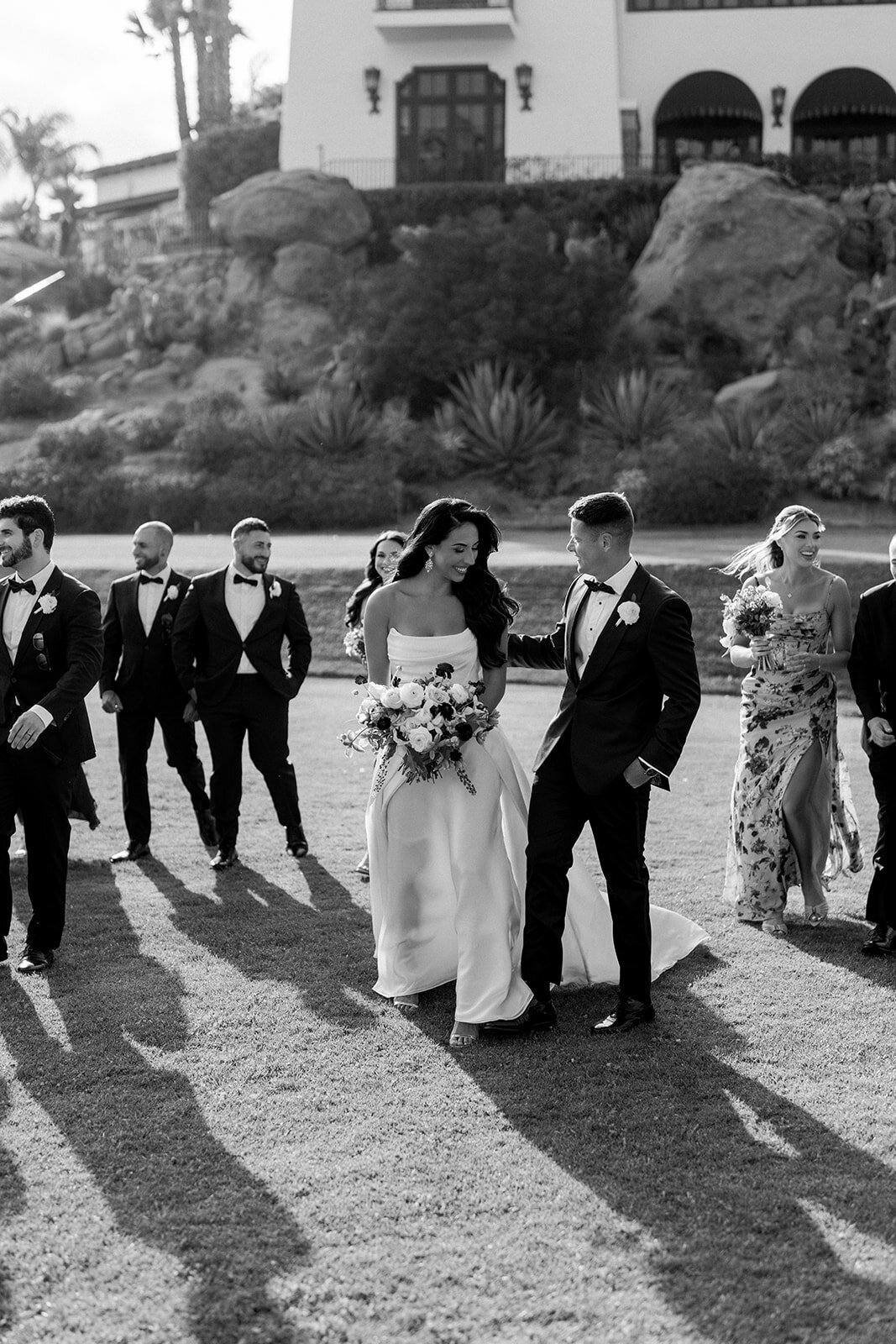 Candid documentary photo of groom leading bride through venue grounds in timeless black and white.