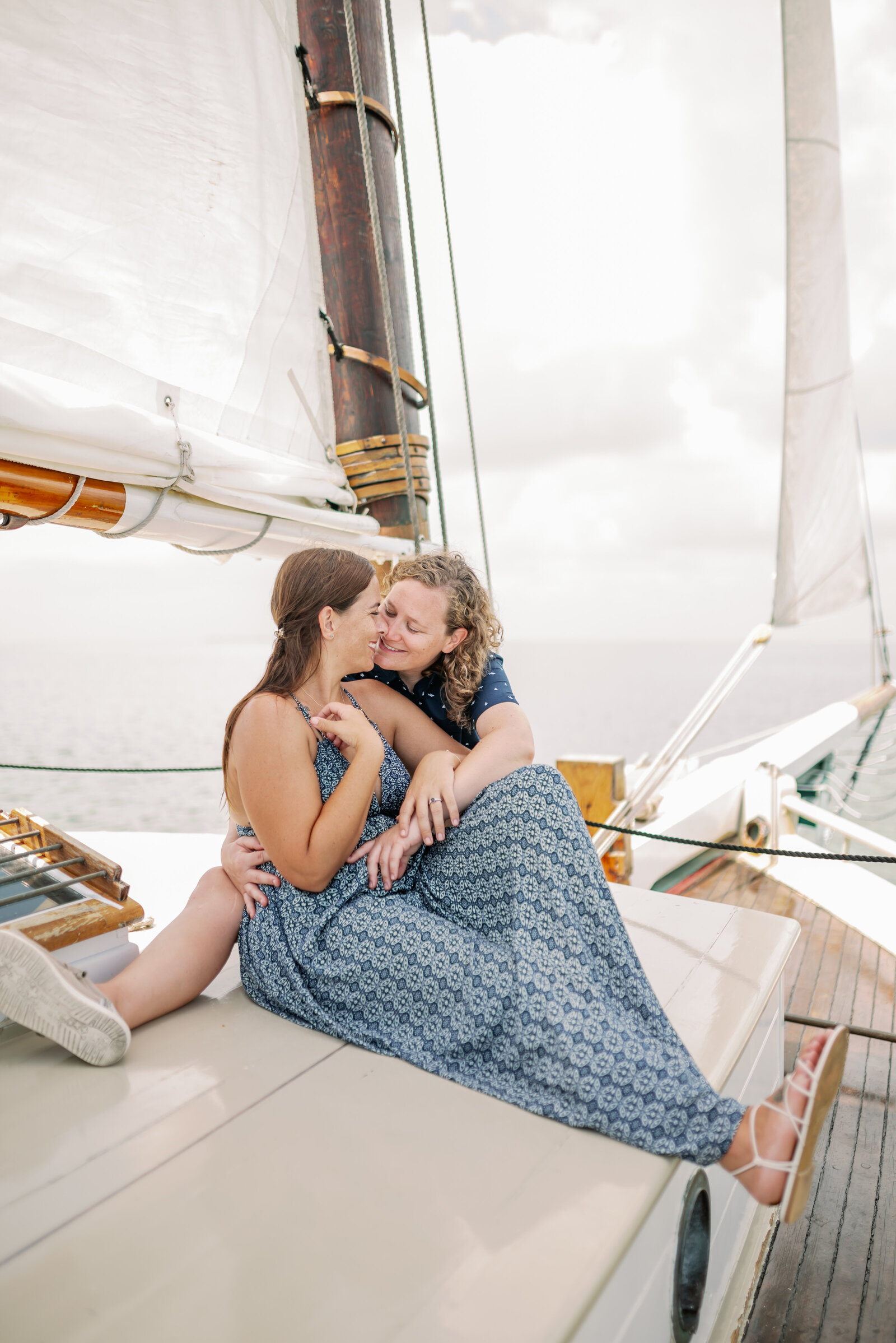 engaged lesbian couple sitting together on a sailboat about to share a kiss