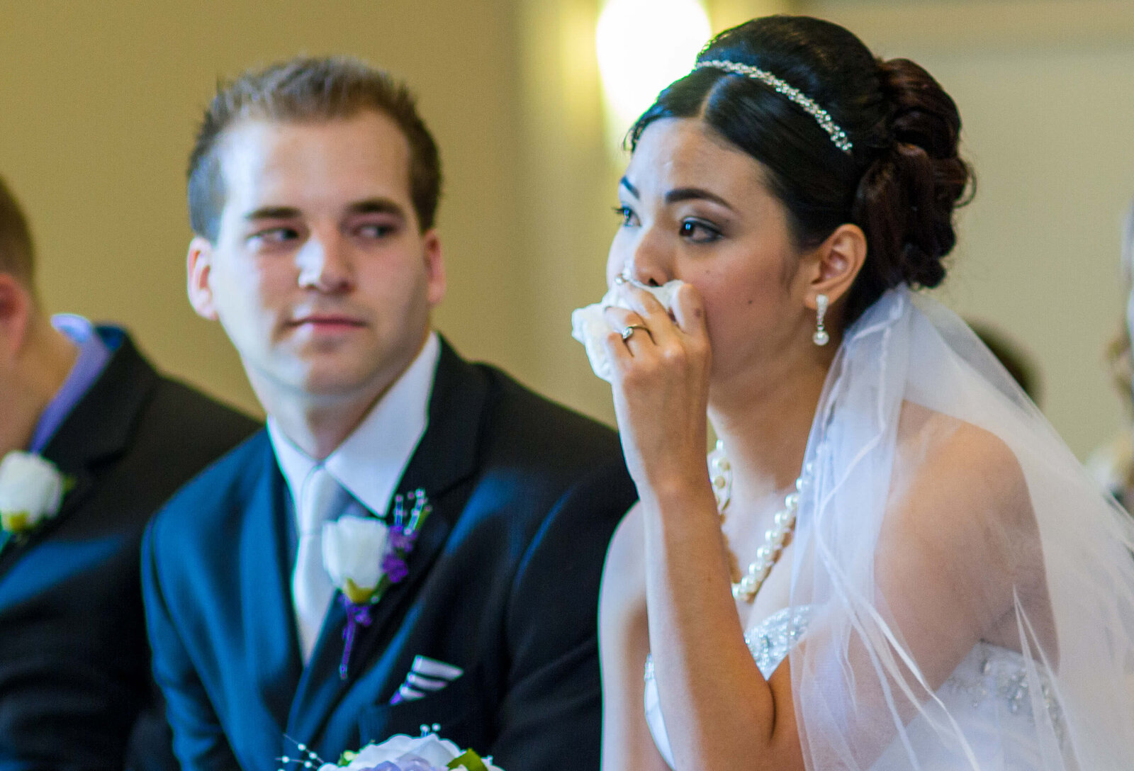 Groom sneaking a peak at Bride  while she  wipes tears from her eyes