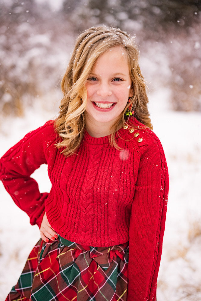 a girl in a red sweater smiles at the camera during a snow storm