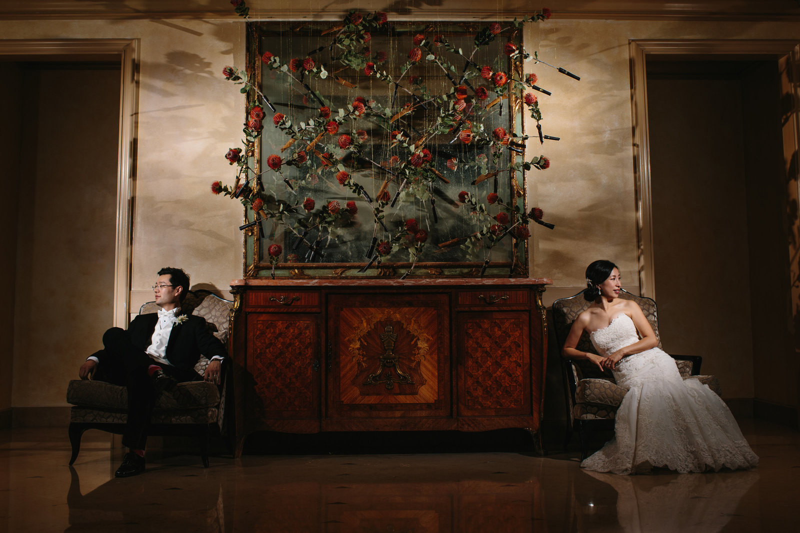 Dramatic bride and groom photo  in hotel lobby sitting on either side of hanging flowers
