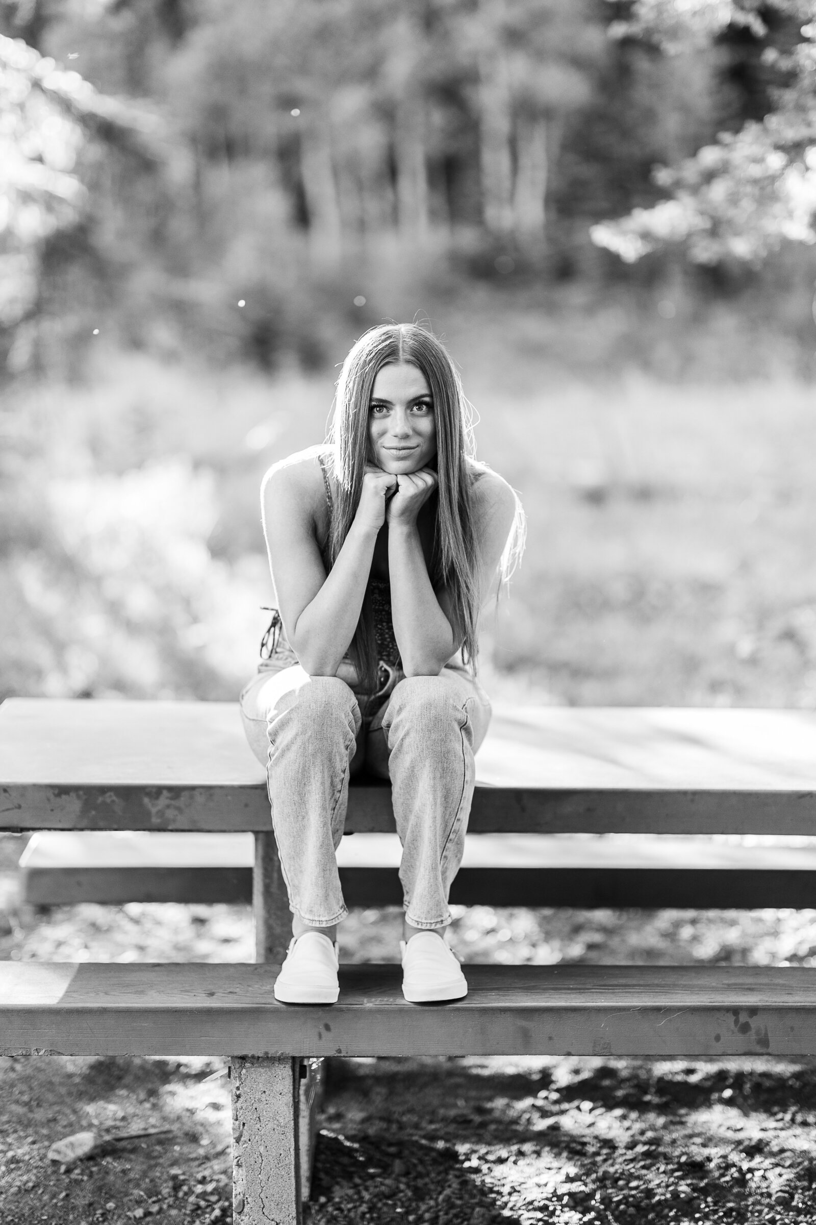 Girl sits on picnic table with hands under chin, leaning forward for senior picture