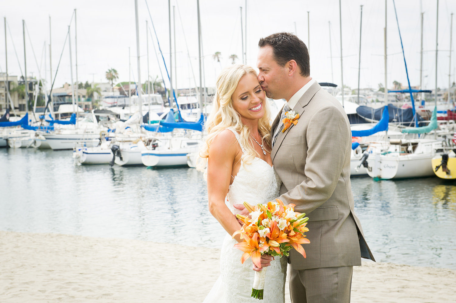 groom kissing brides head with boats in the background