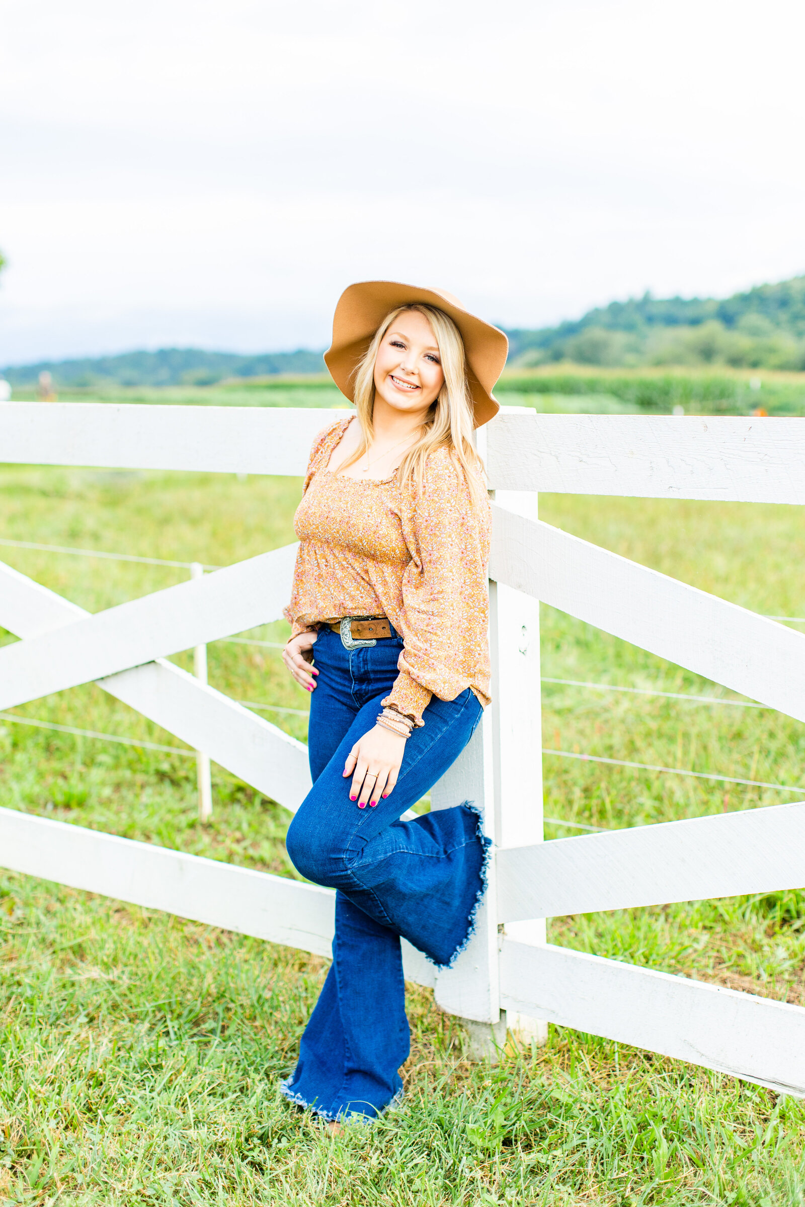 girl with jeans and brown hat leaning on white fence at Antler Hill Village