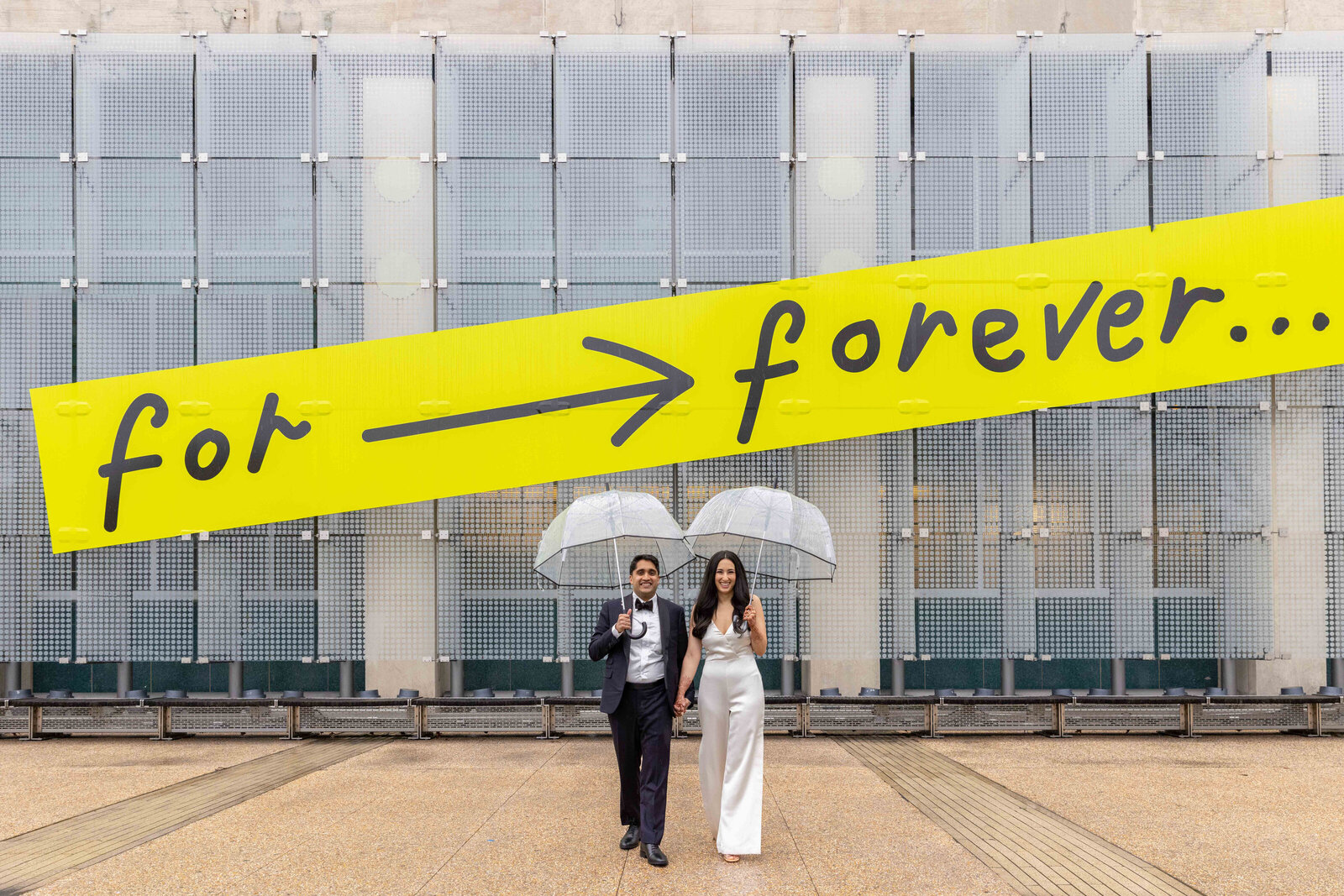 A wedding couple walking together while holding clear umbrellas.