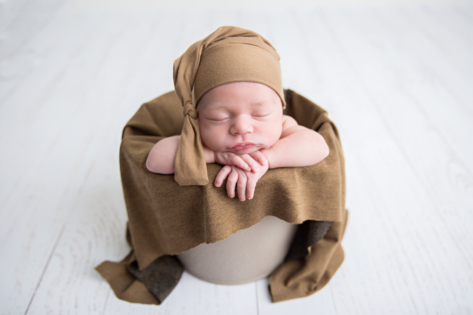 sleeping newborn baby in bucket with brown sleepy cap