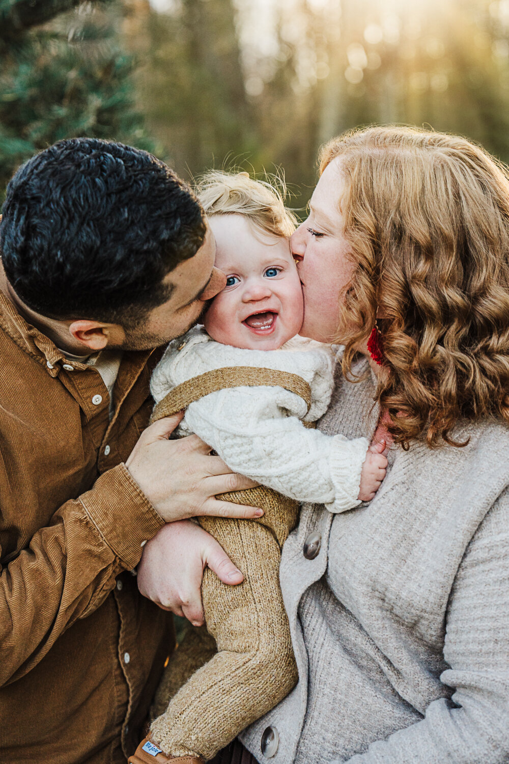 mom and dad kiss the cheeks of toddler boy in overalls at a tree farm