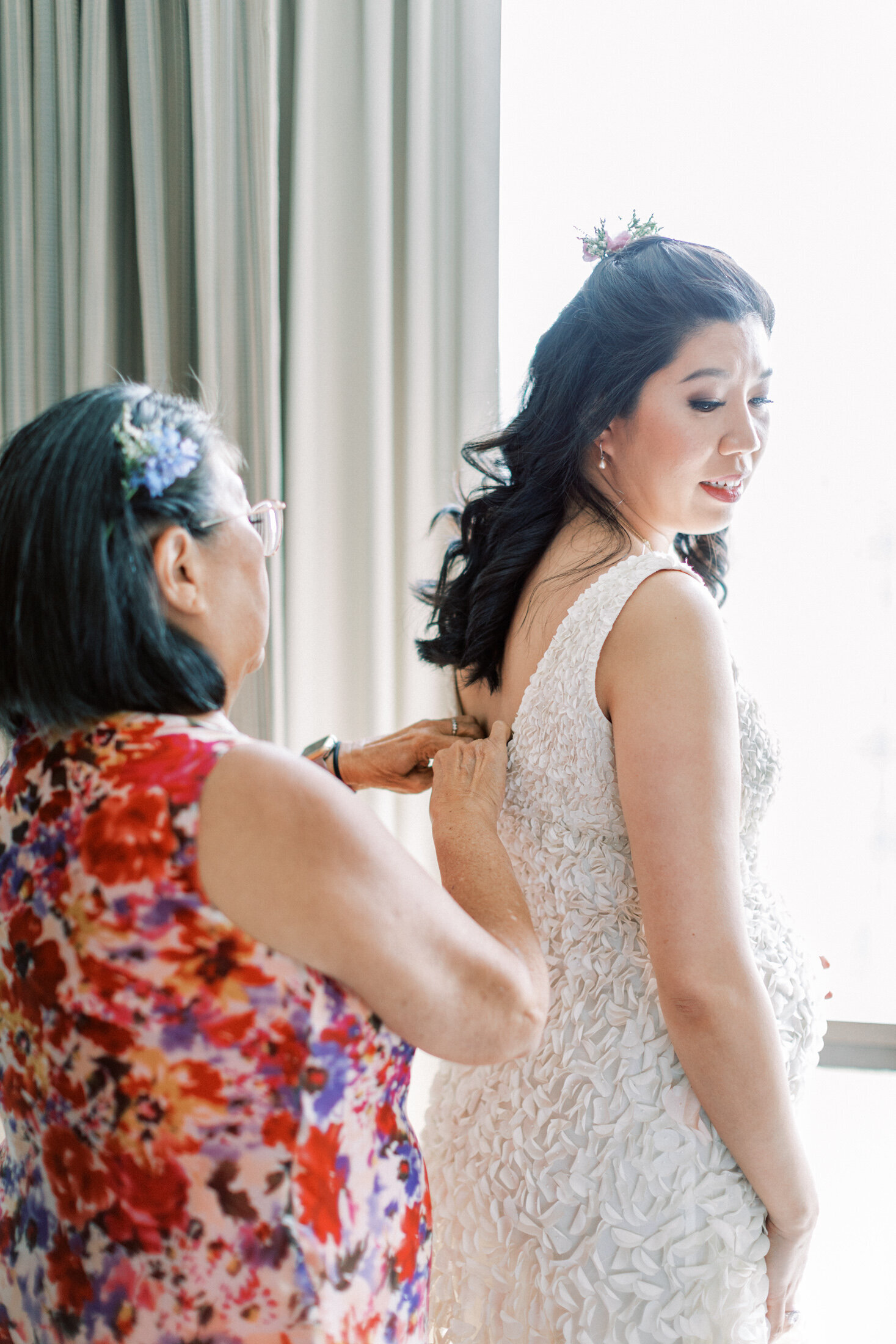 Bride gets ready as mom helps her button her dress
