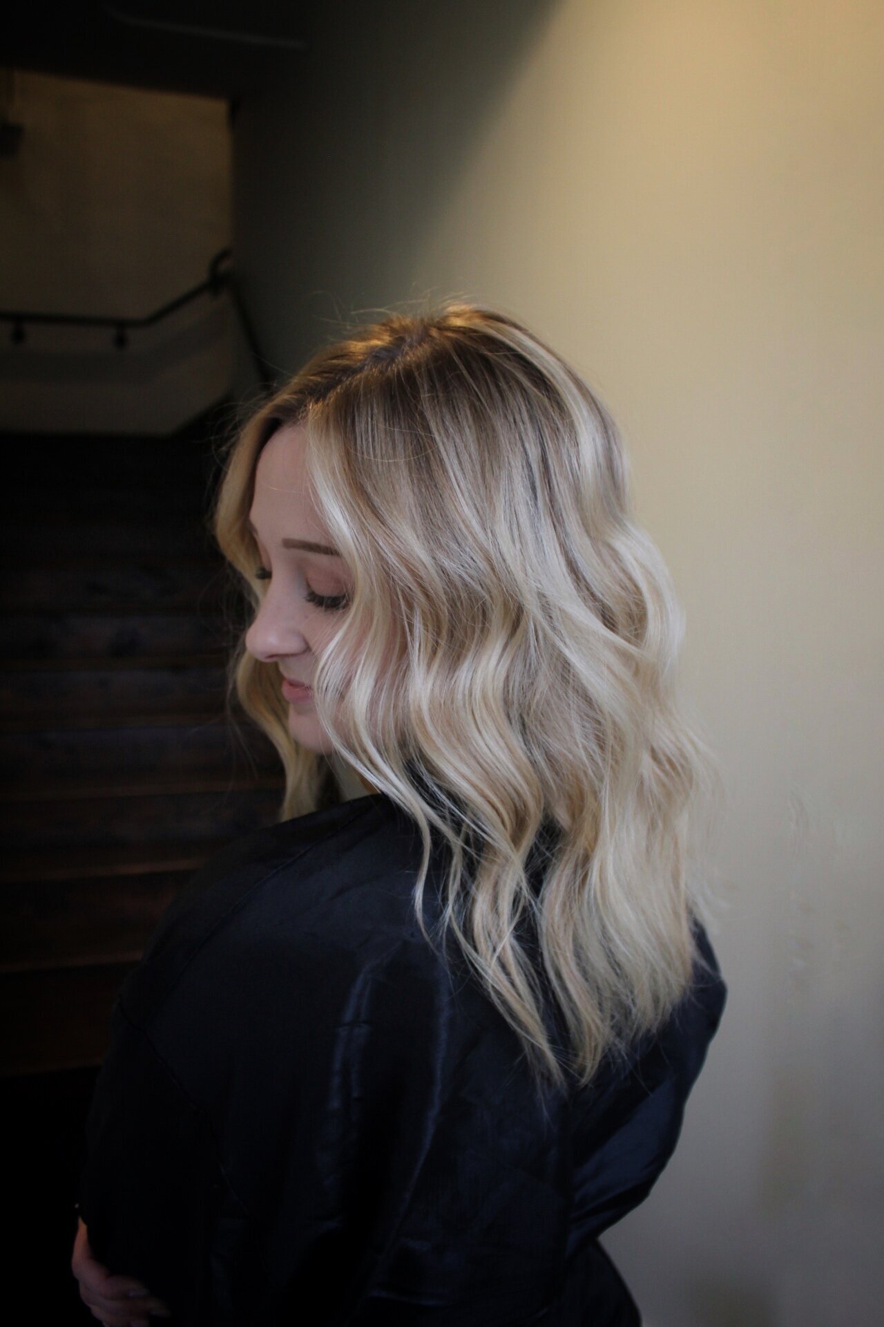 Our satisfied client with blonde wavy hair looking down, showing off her hairstyle