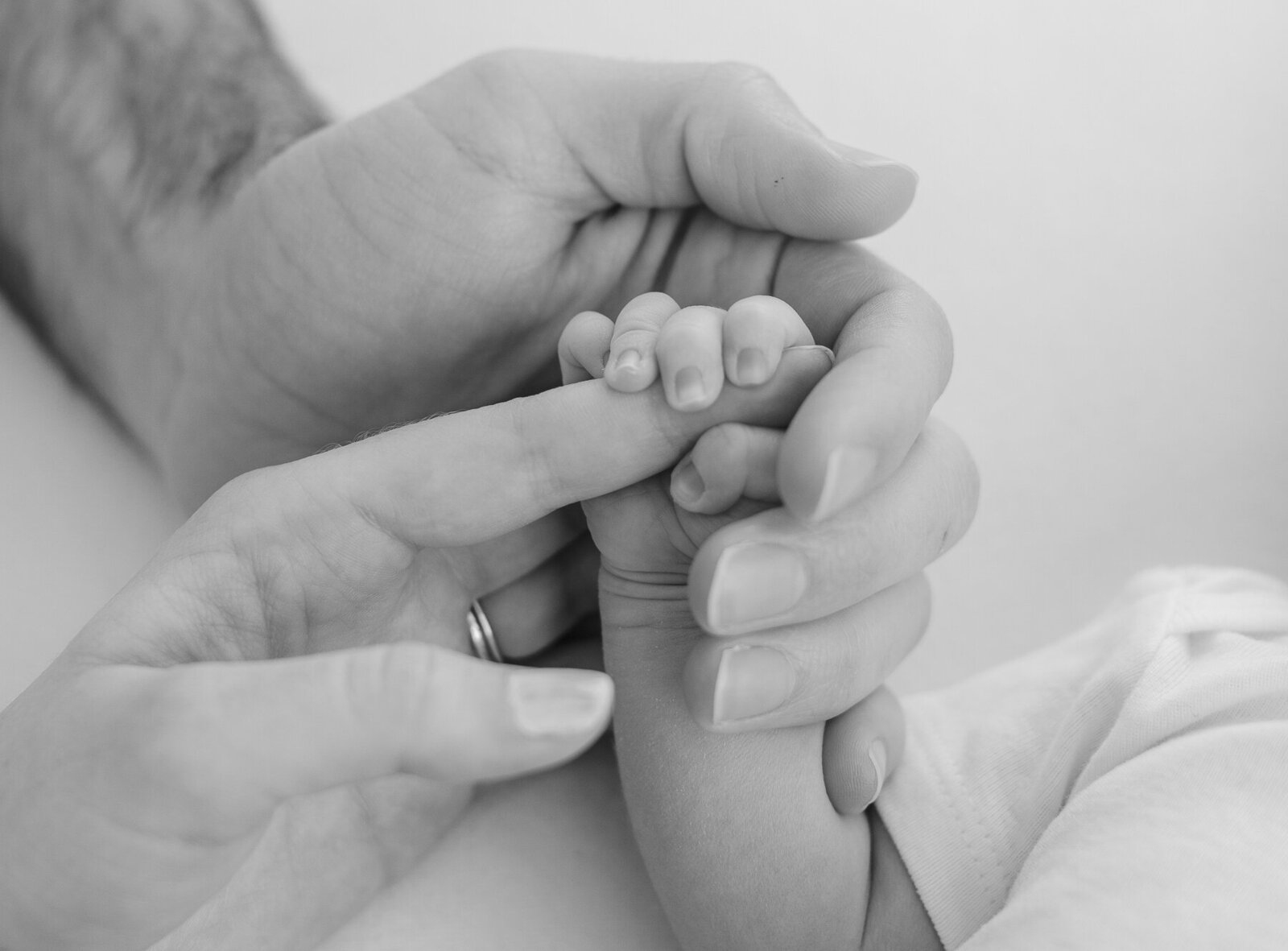 black and white close up of mom and dad hands holding newborn baby's hand