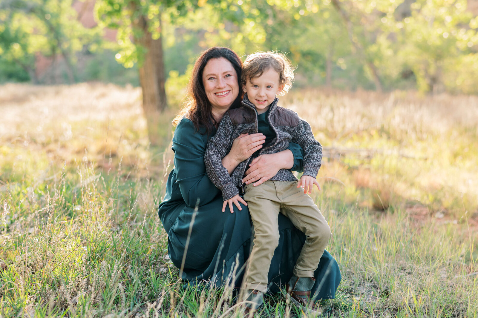 A stylish mother and son sit in a field together at sunset and smile at the camera of Northern Virginia family photographer