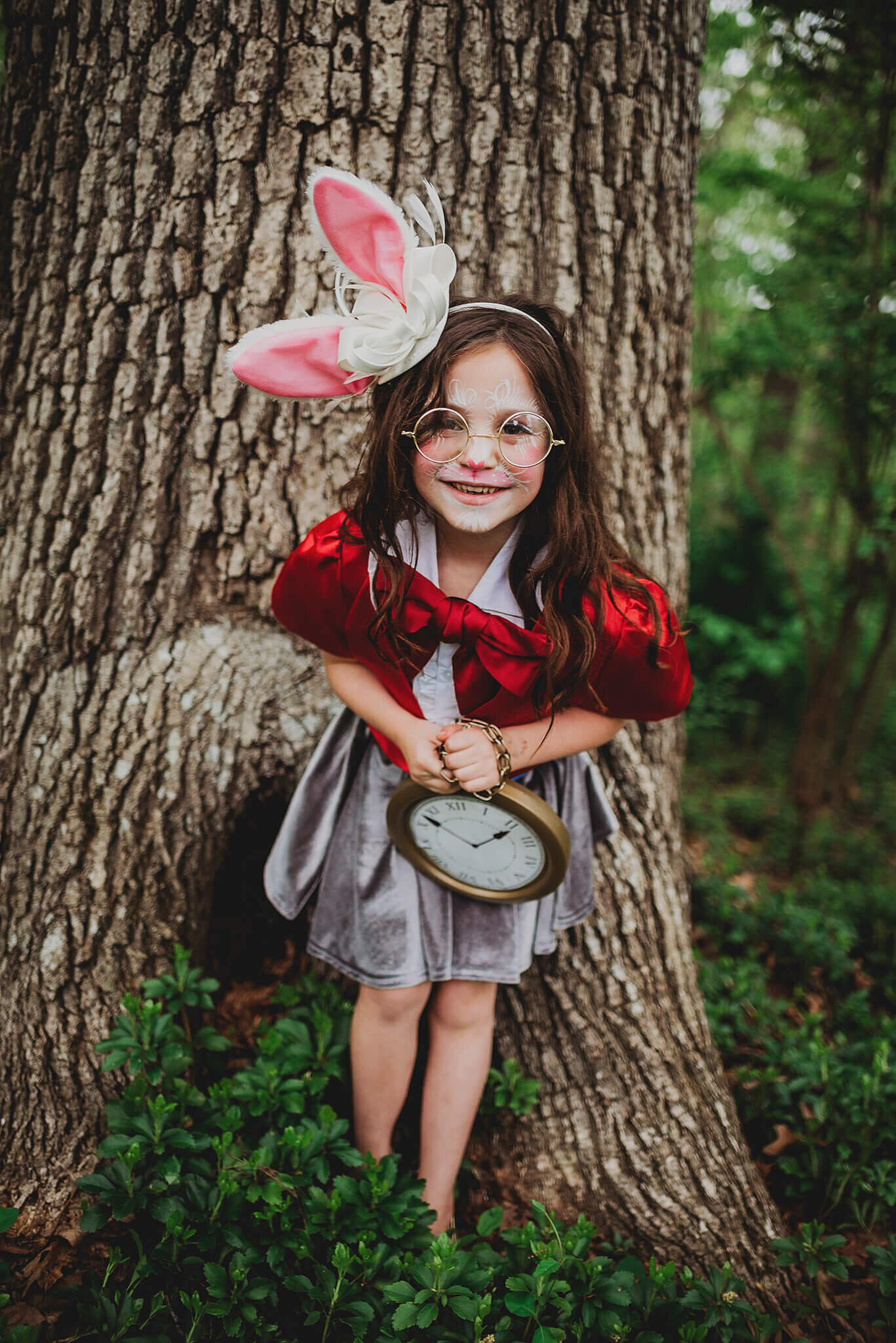 Girl in rabbit ears with red jacket and grey skirt leaning up against a tree