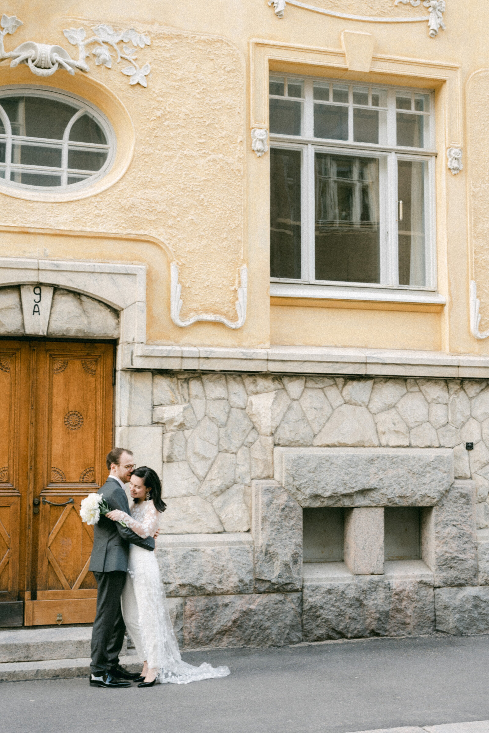 A wedding coulple photographed by  the wedding photographer Hannika Gabrielsson in front of  a yellow building in Helsinki.