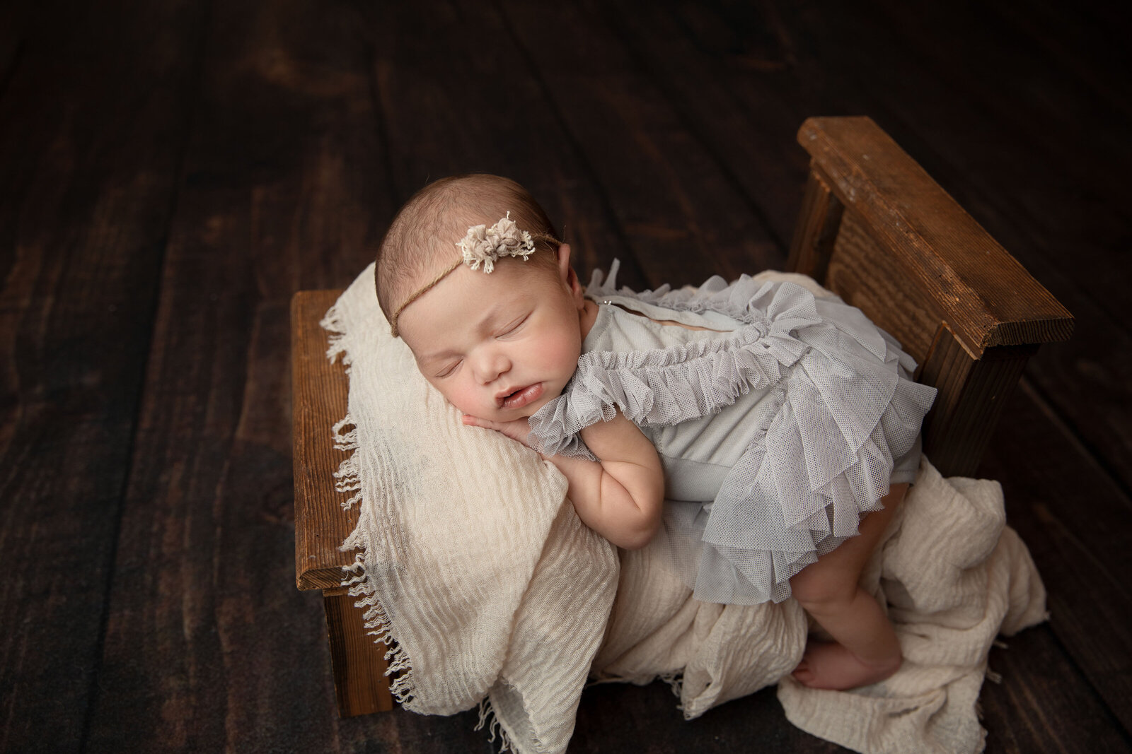 newborn session with gray lace romper in brown wood bed