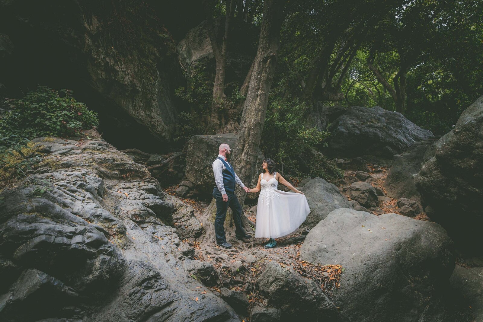 A couple looks at each other and holds hands as they pose for forest portraits while eloping.