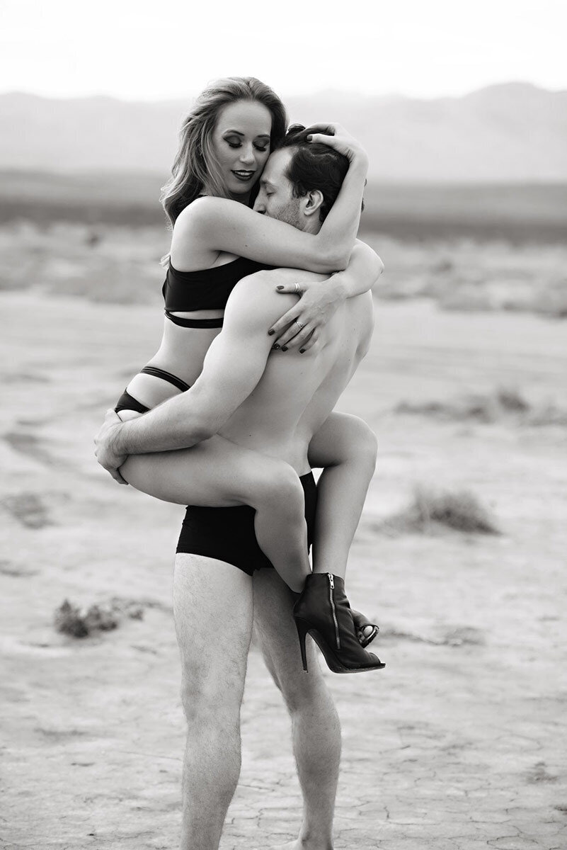 Black and white boudoir portrait of woman being held by her partner in the desert