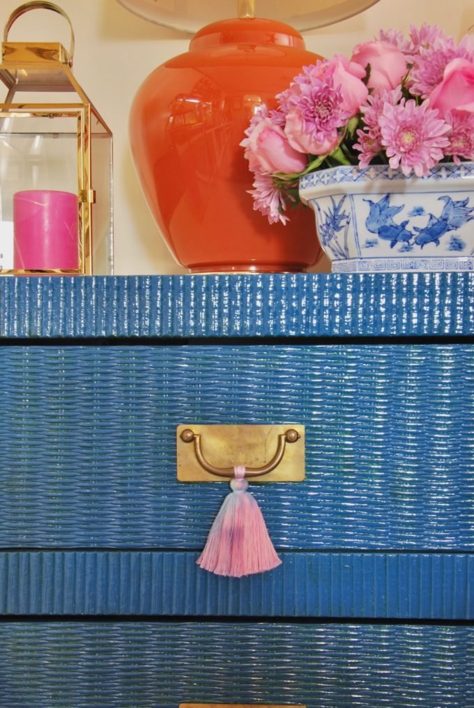 A blue wicker table with brass pull and pink tassels.