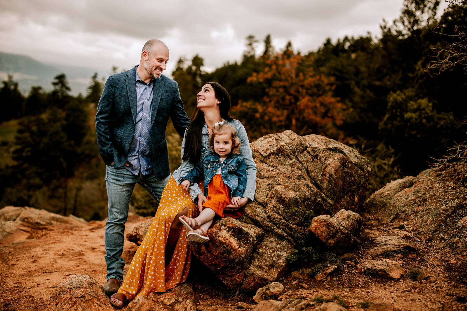 family of three pose on rocks in mountains for  family photos in morrison colorado