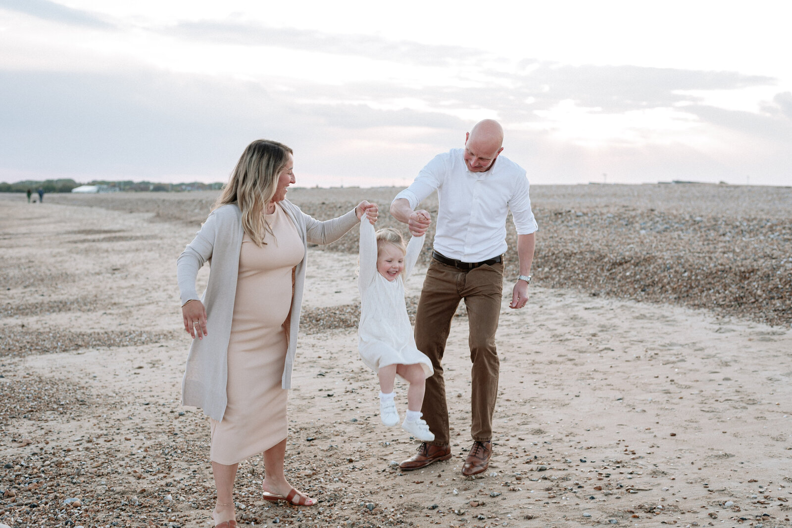 Mum and dad walking with little girl and lifting her up with their hands at family photoshoot in west sussex