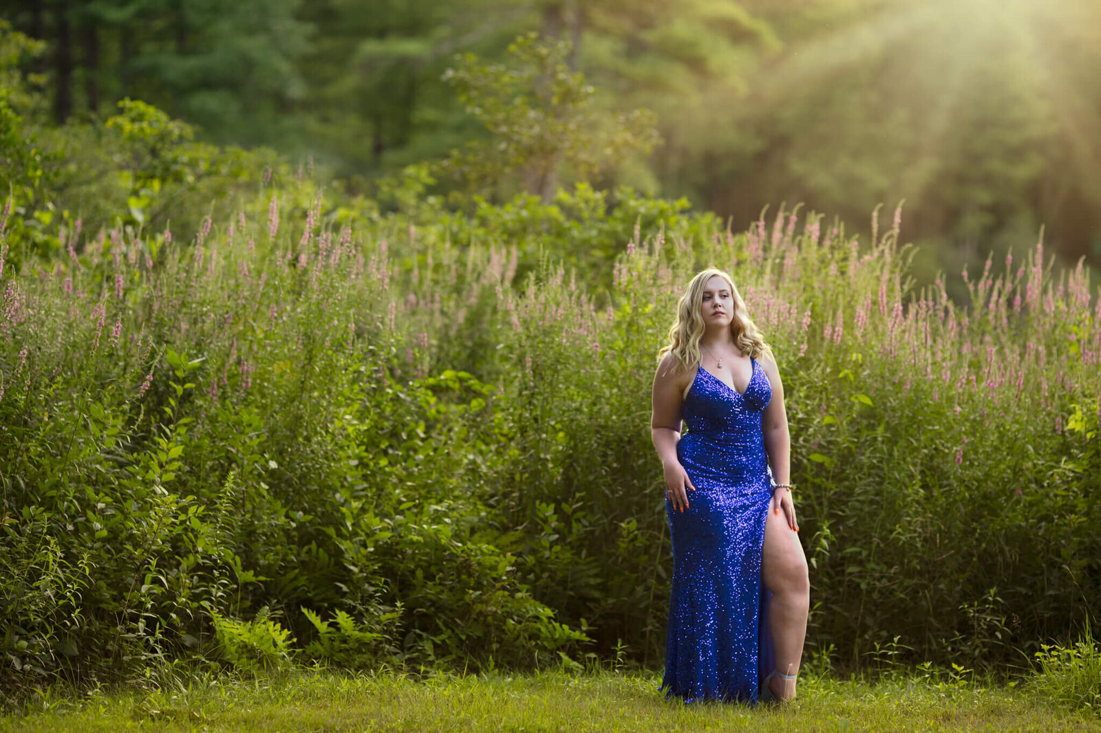 High school senior portrait of a female in a blue sparkling dress with tall flowers in the  background