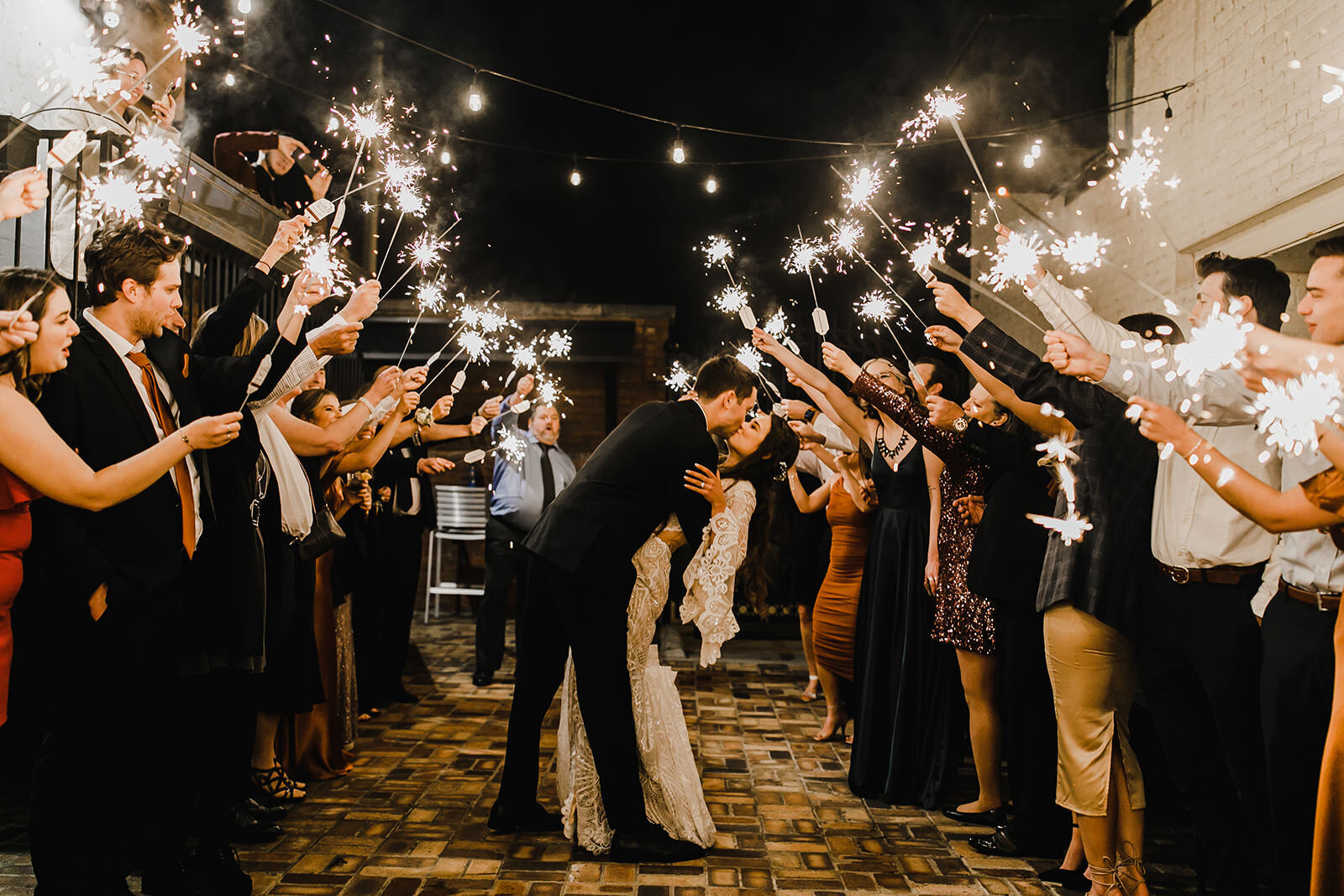 bride and groom kissing with guests on either side holding sparklers