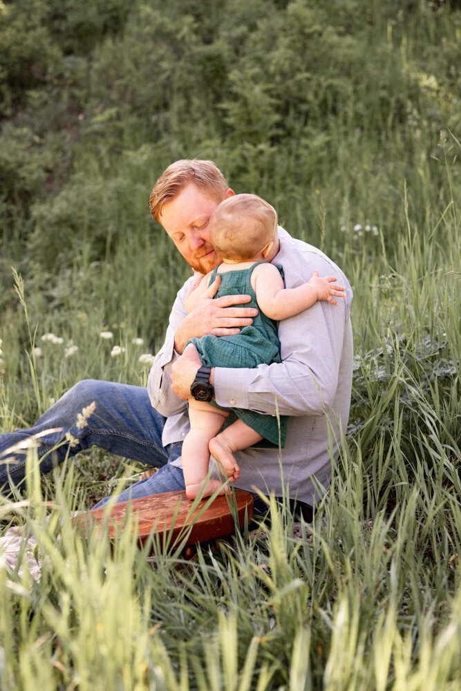 a dad gives his daughter a hug in a mountain meadow