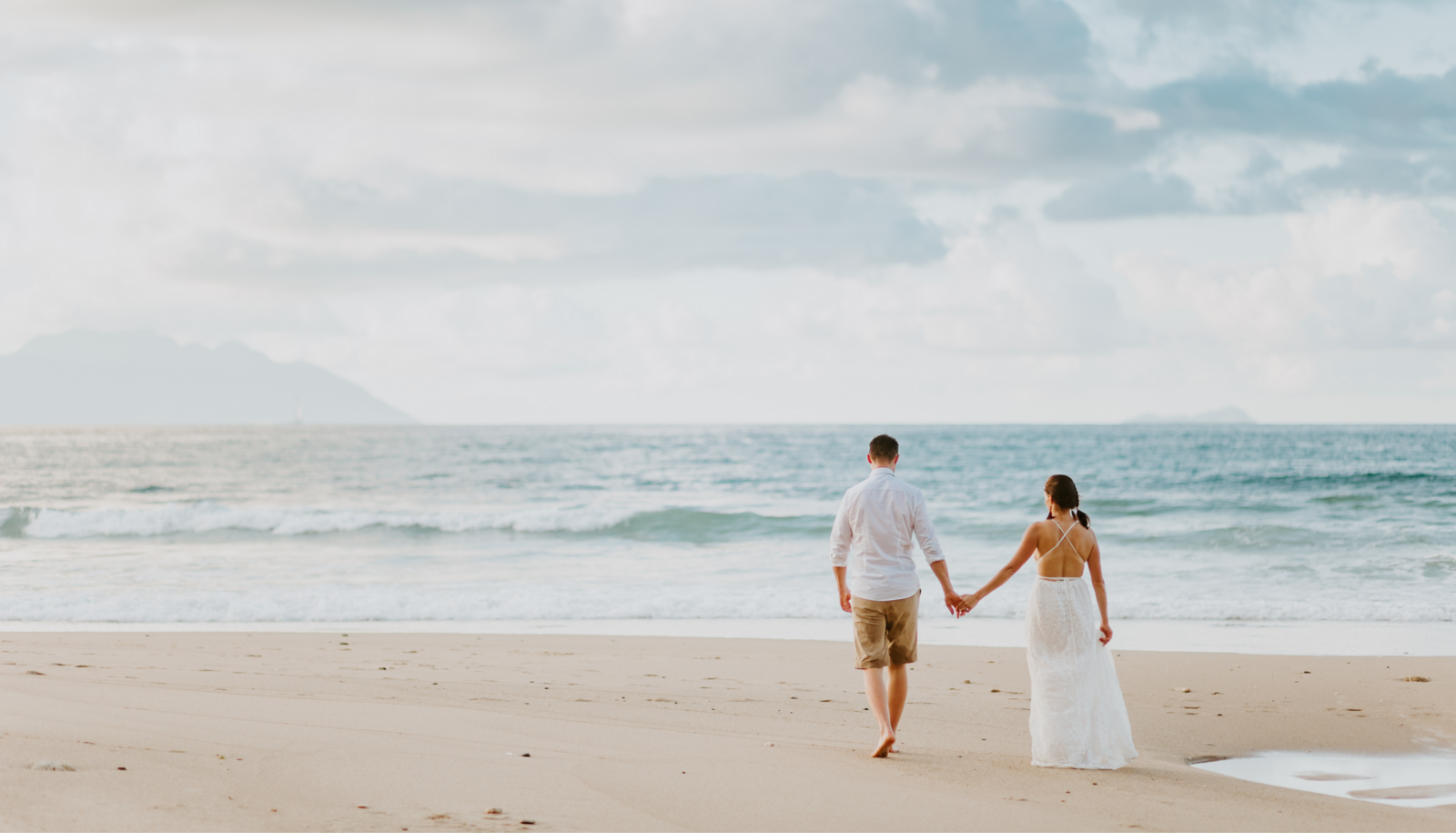 A Bride and Groom walking on the beach holding hands.