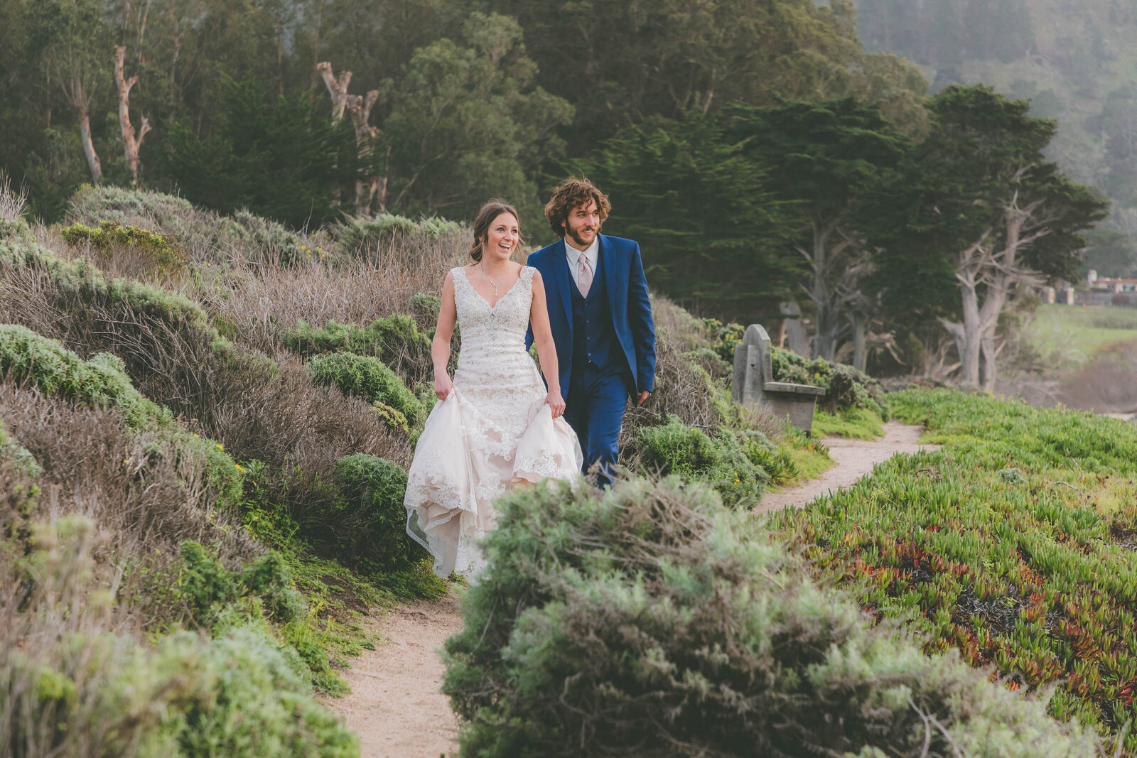 A couple in wedding attire hikes down a path in Carmel.