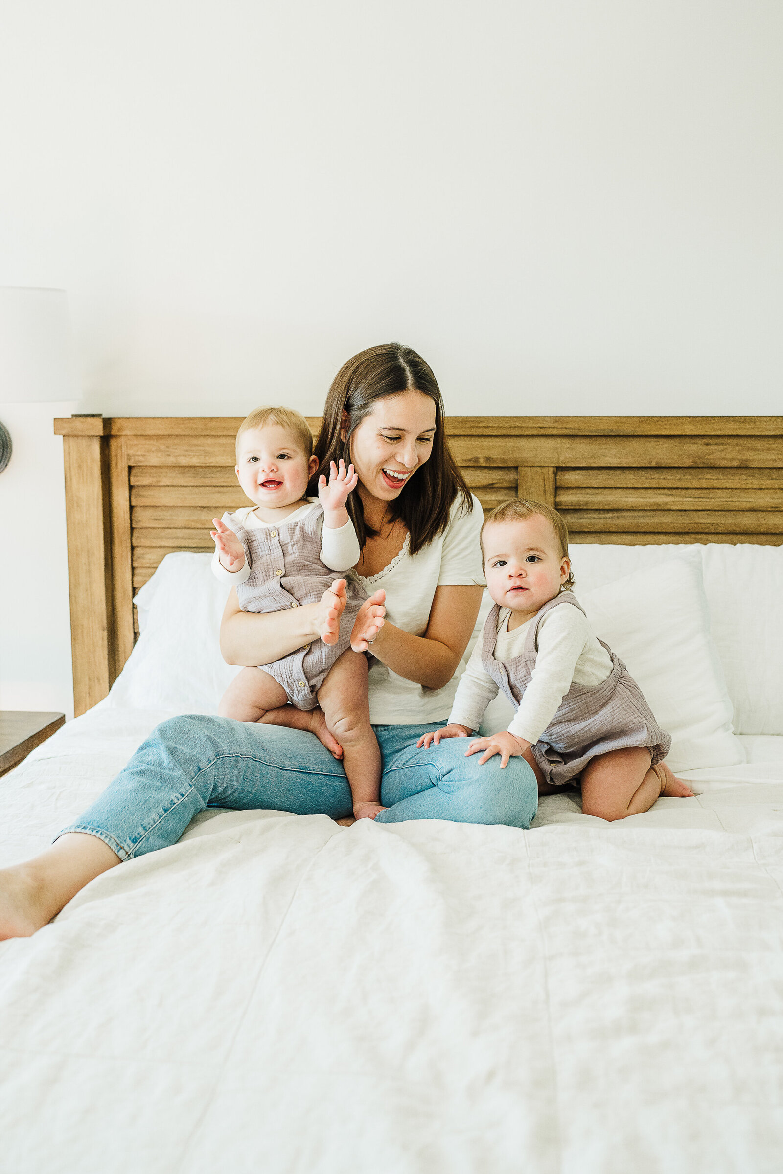 mom laughs with twin toddler girls on bed