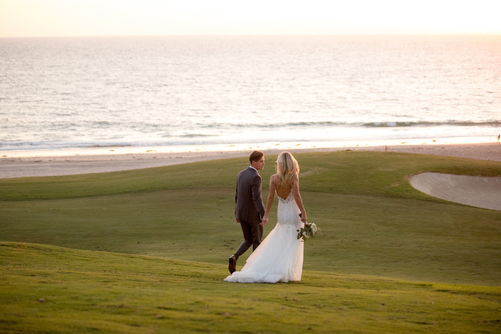 bride and groom walking on golf course with beach view