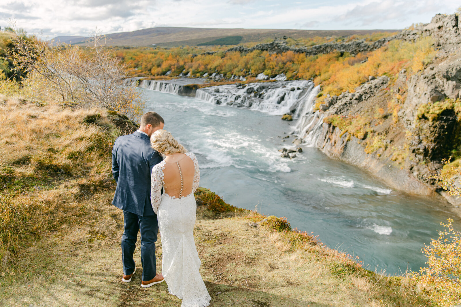 bride and groom with their back to the camera and looking at the waterfalls in iceland