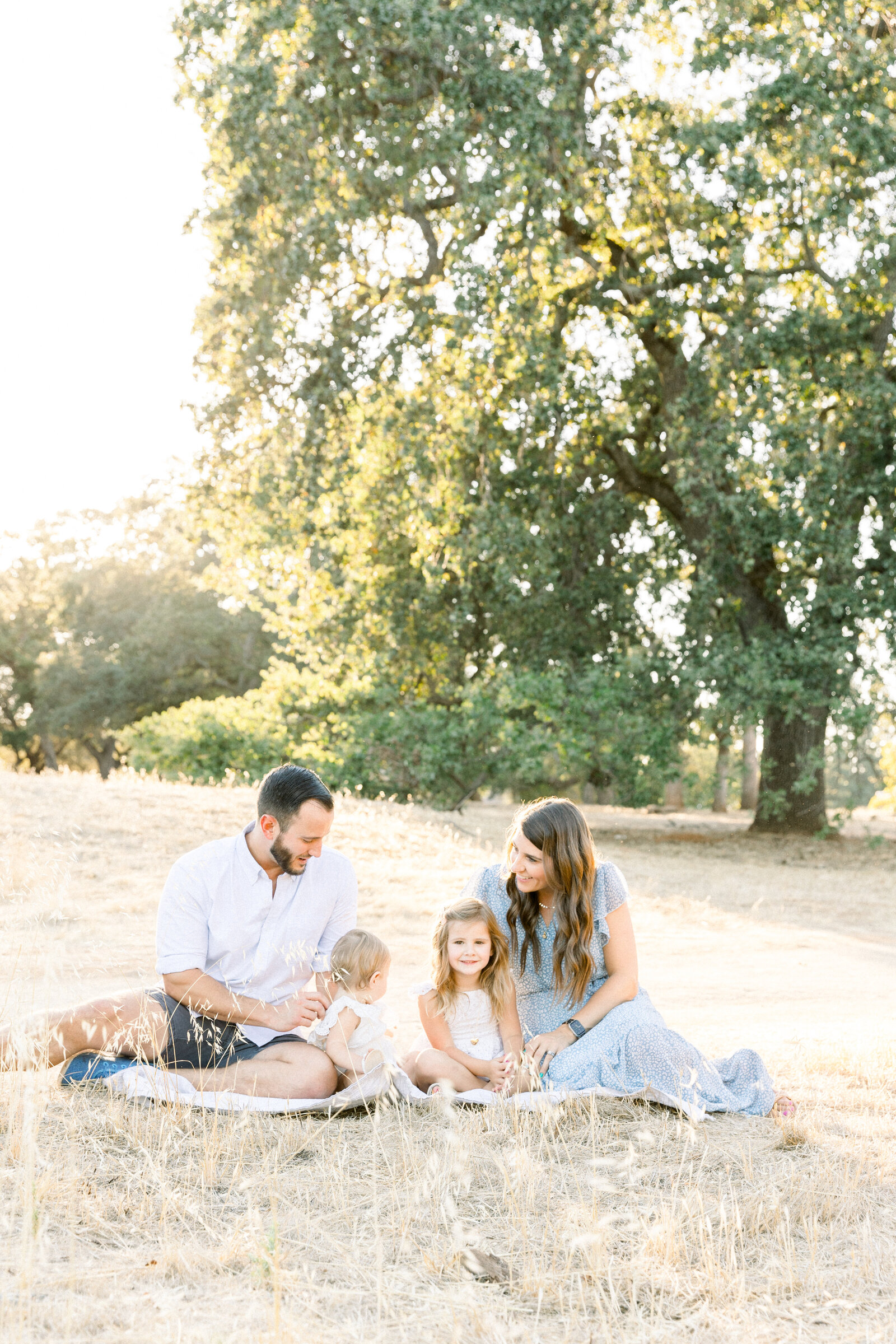 Image of young family sitting on a blanket in a field together taken by Sacramento Newborn Photographer Kelsey Krall