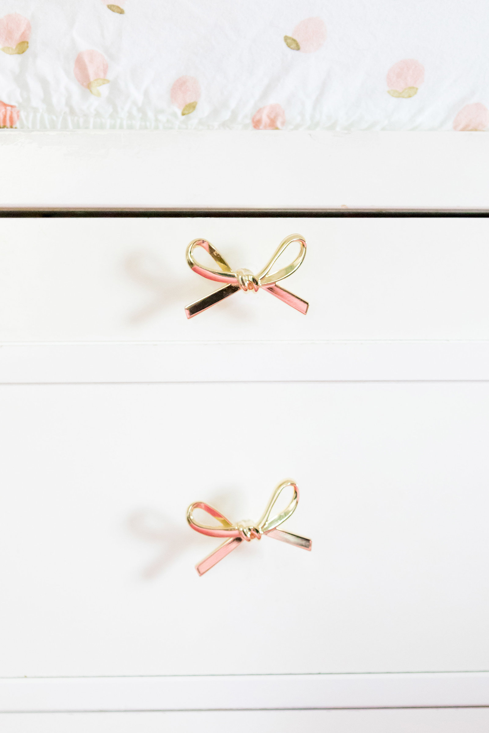 A white dresser changing table with rose gold bow pulls.