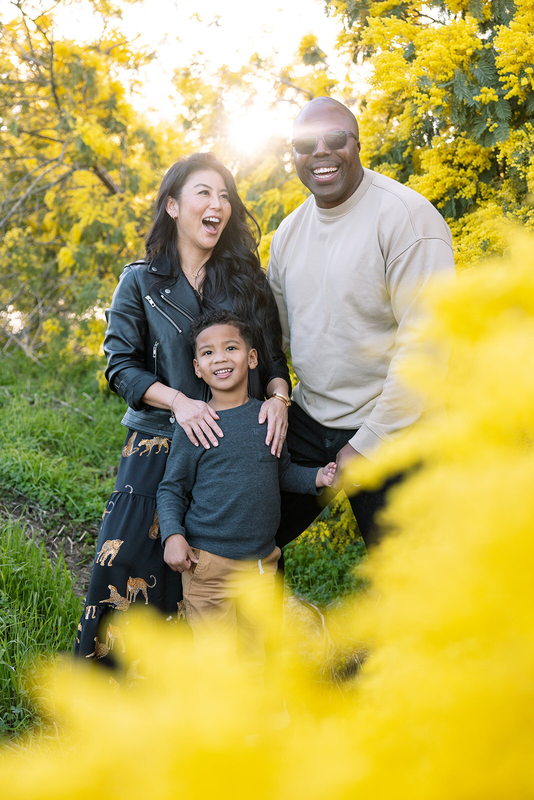 mixed race family of three smiling outdoors surrounded by blooming acacia trees