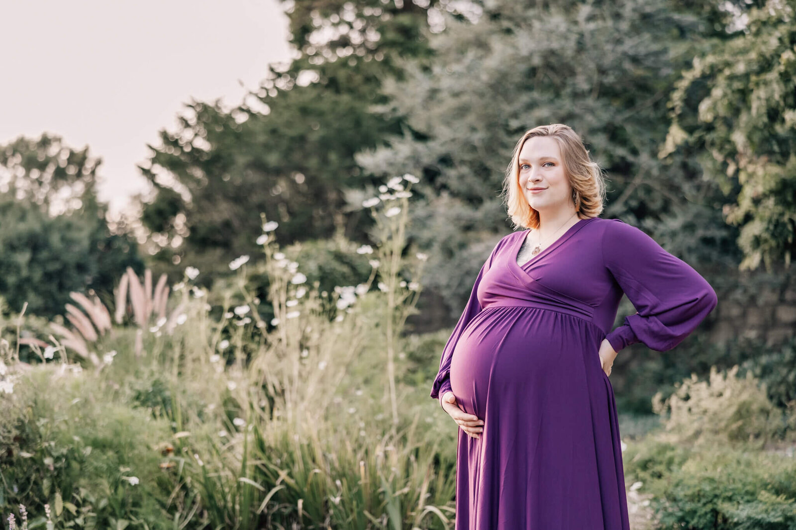 Pregnant woman holds belly in purple dress in flower garden