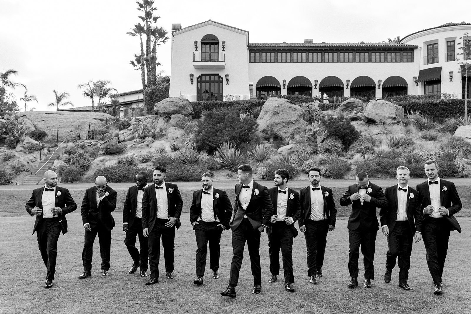 Groomsmen walk in formation across venue grounds in classic black tie at Hummingbird Nest Ranch, photographed in documentary style.