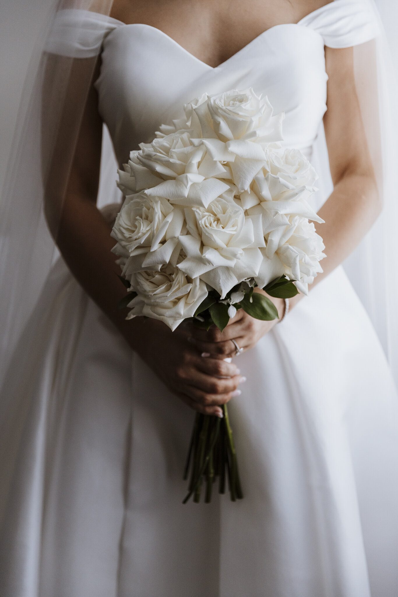 A white rose wedding bouquet held by a woman in a white dress