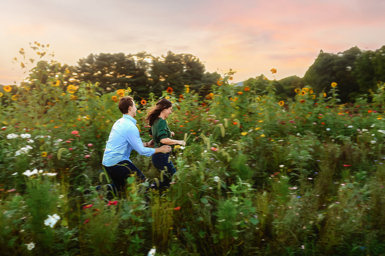 A couple in love playfully chases each other for Engagement Photos in a field of flowers inAsheville, NC.