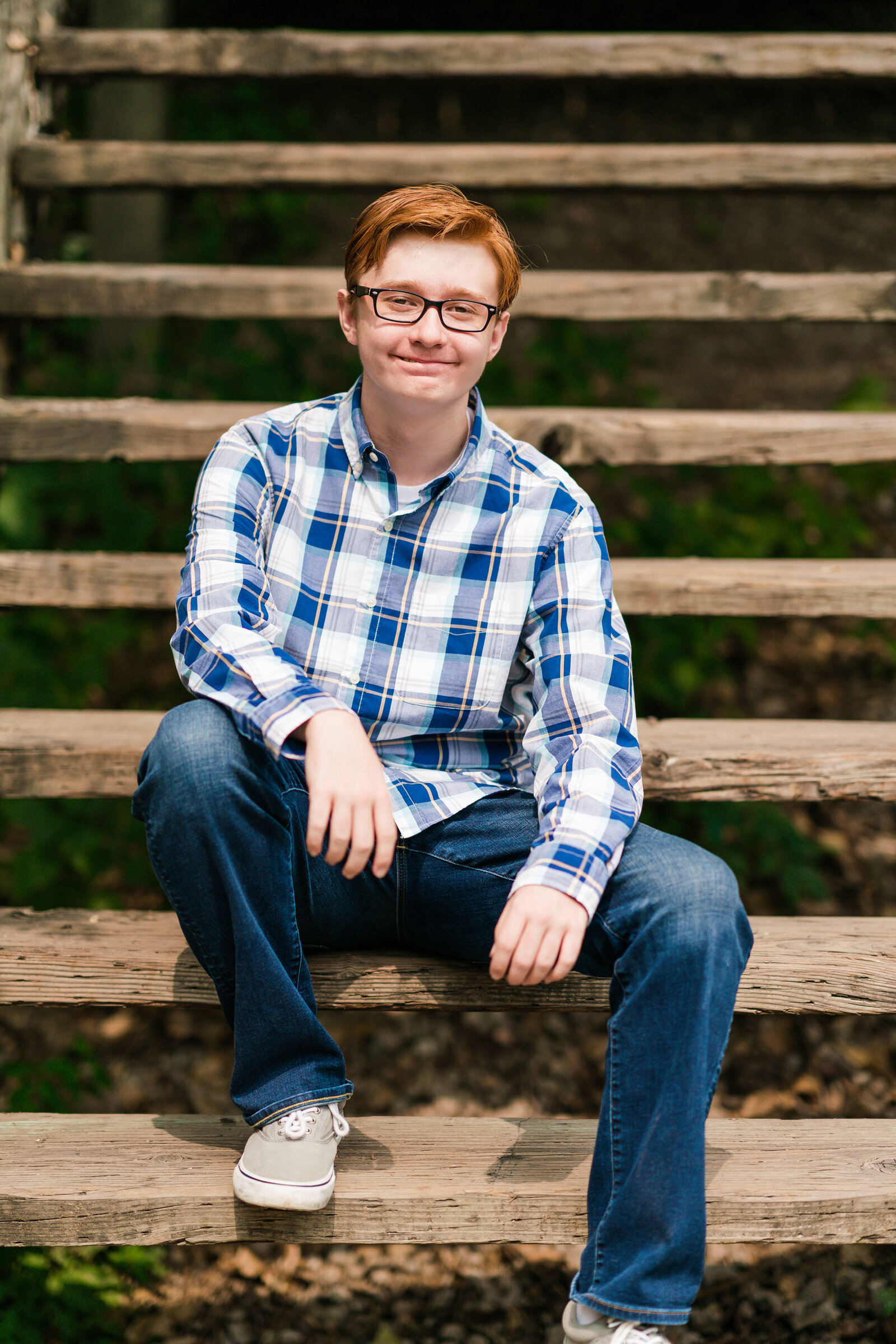 Senior boy dressed in flannel and jeans sits on the stairs.