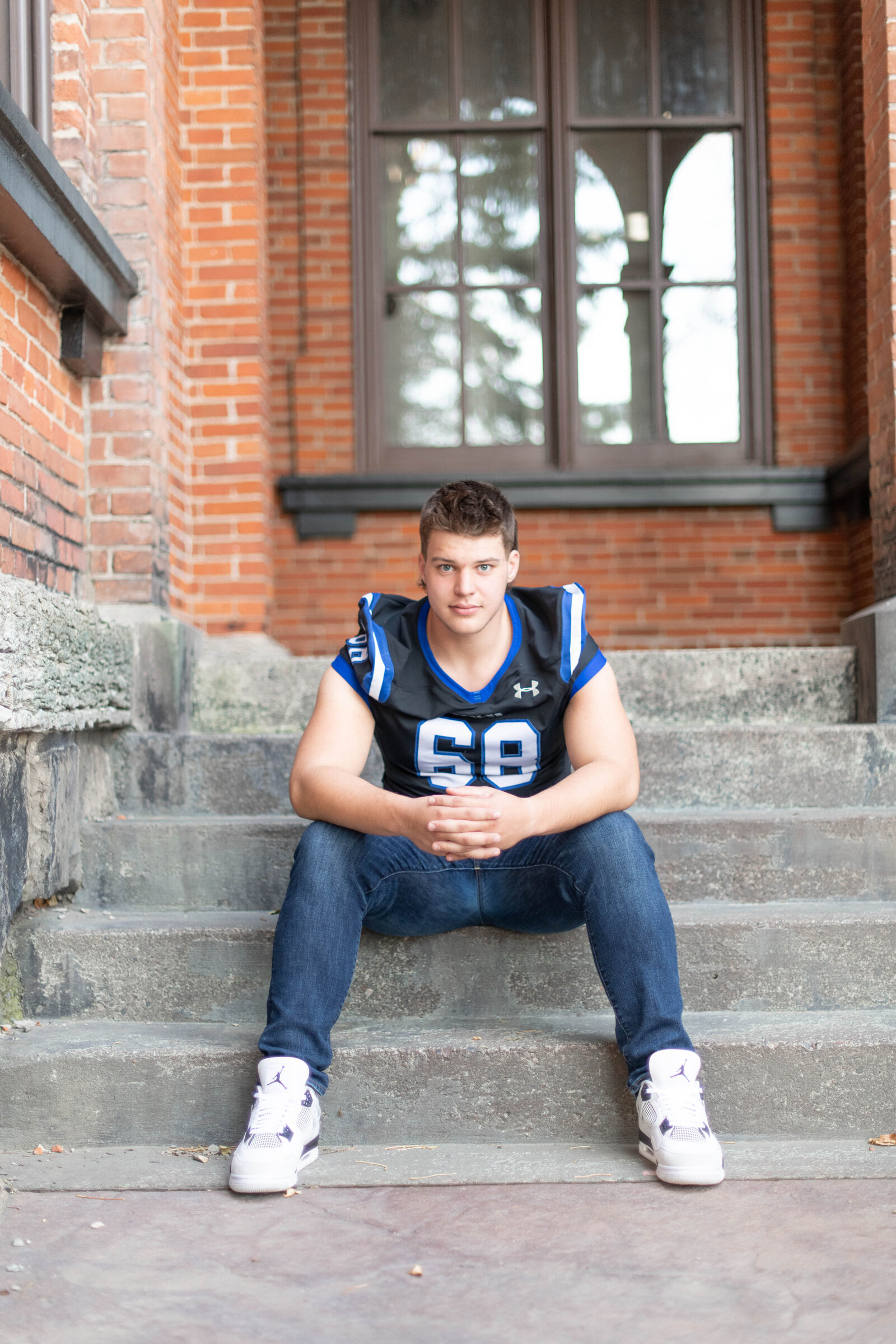 senior boy sitting on steps in football jersey