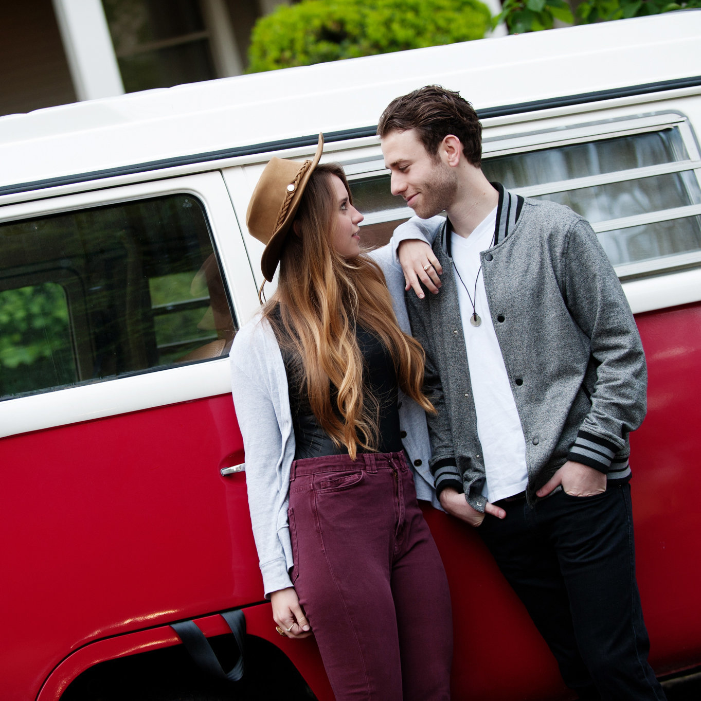 a stylish man and woman stand close in front of a vibrant red and white vw bus