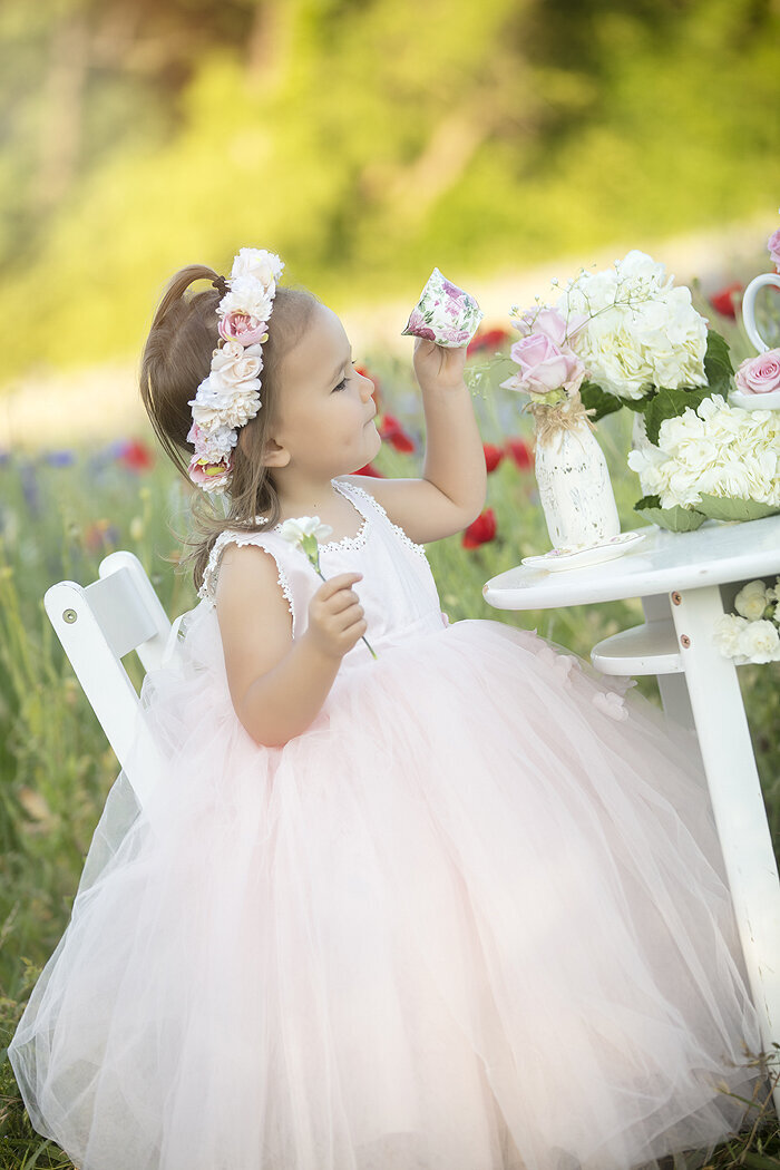 Little girl sitting at table for tea party in Richardson wildflower field, a Dallas child photographer.