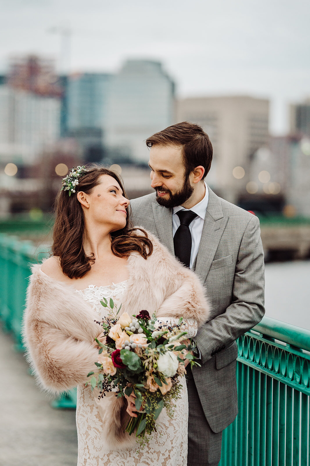 wedding couple dressed for winter pose by green fence in boston