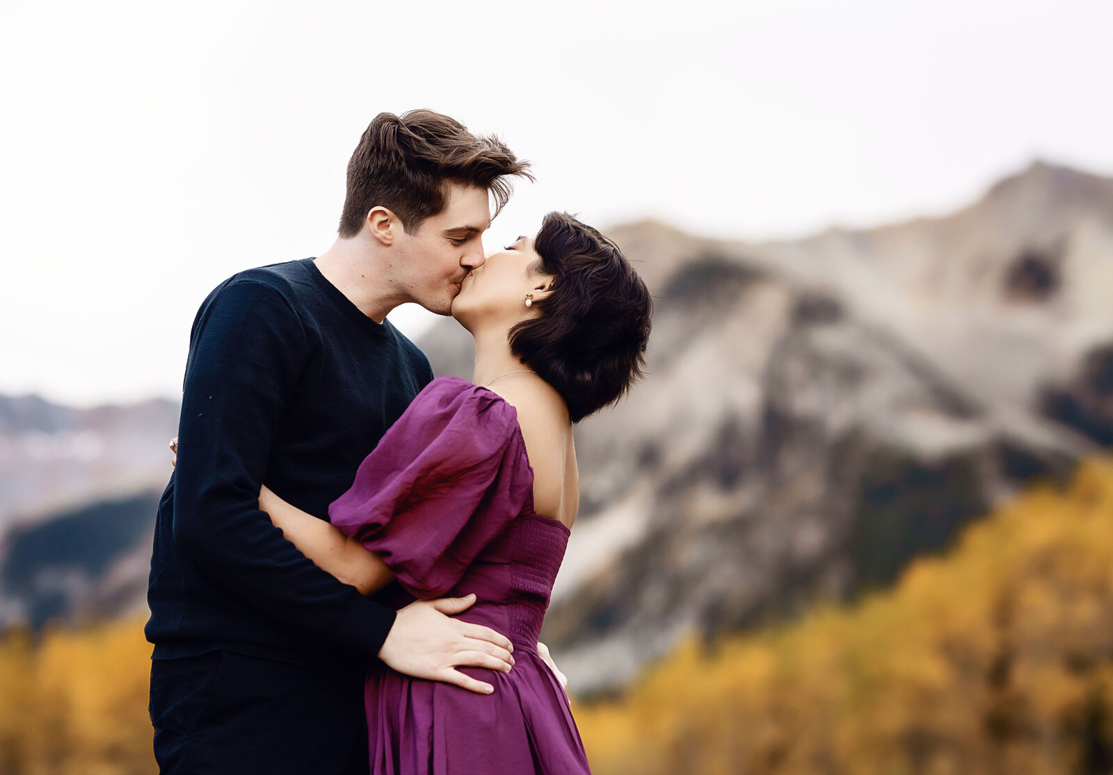 A man kisses his fiance with the aspen yellow trees behind him,
