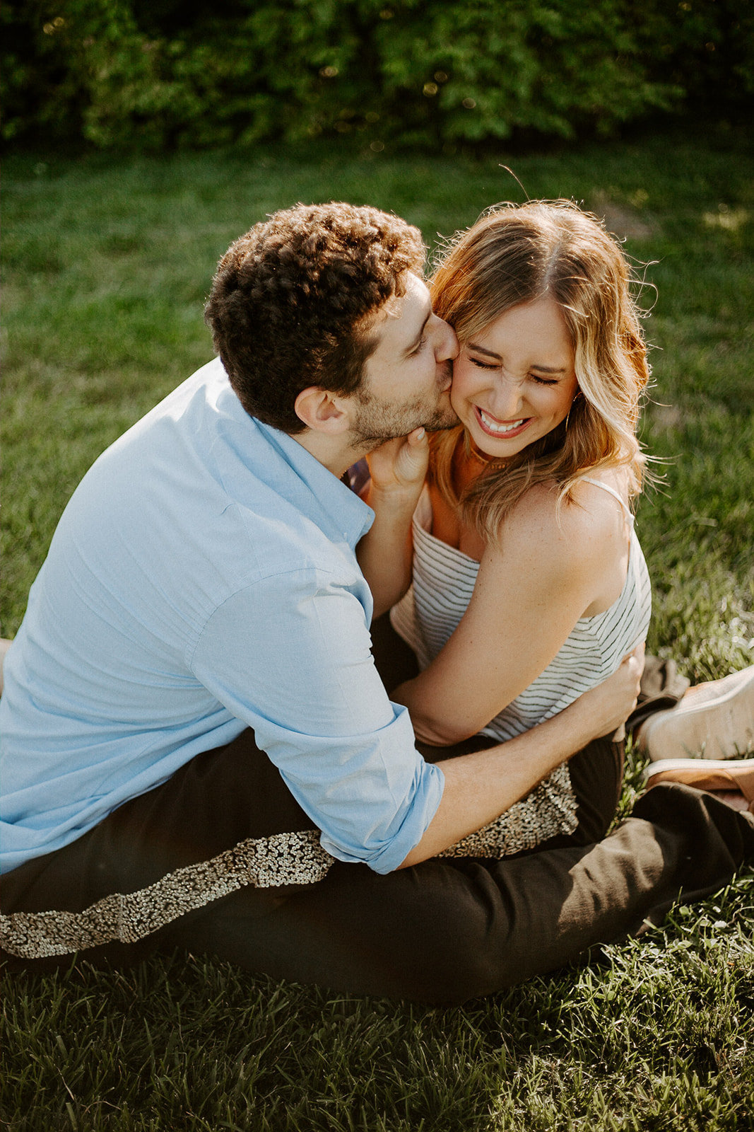 Couple cuddling together in the grass with the man kissing his fiance on the cheek during their Minneapolis Engagement Session