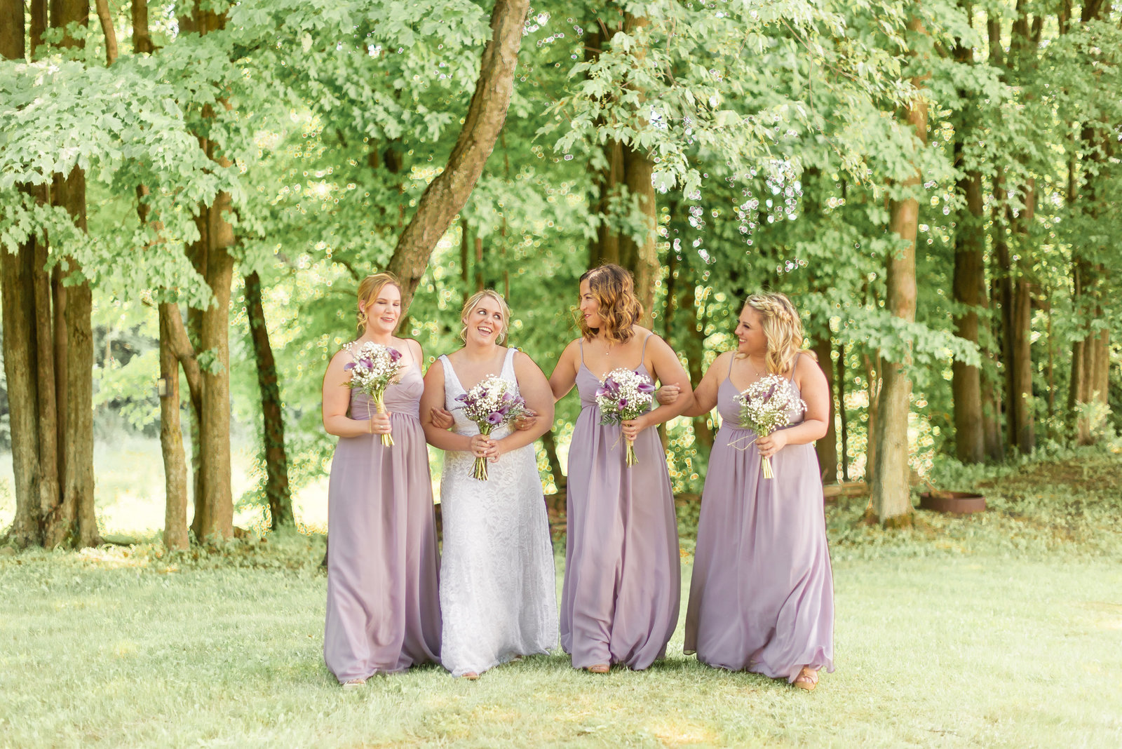 Bridesmaids in lavender dresses walk with the bride