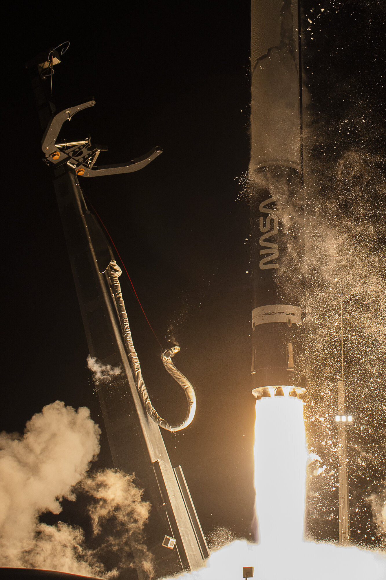 Rocket Lab's Electron rocket. Leaving the launch pad. Pad dramatically lit by engine fire, Nasa Logo on fuselage.